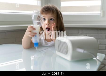 una bambina ha paura di usare un nebulizzatore: il bambino tiene una maschera nelle mani e non vuole inalare Foto Stock