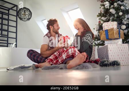 giovane coppia seduta sul pavimento in font di albero di natale accanto al mucchio di regali. femmina sorpreso dal dono di un maschio ardito Foto Stock