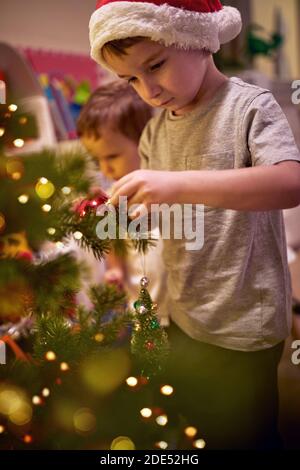 I bambini si sono concentrati sulla decorazione di un albero di Natale a casa in un'atmosfera di vacanza. Insieme, Capodanno, famiglia, celebrazione Foto Stock