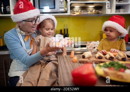 Nonna e nipoti preparano il pasto di Natale in cucina in un'atmosfera allegra insieme. Natale, famiglia, insieme Foto Stock