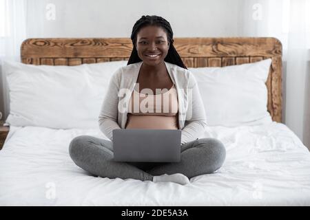 Lavoro a distanza per donne incinte. Black expectant Mamma che usa il notebook a casa Foto Stock