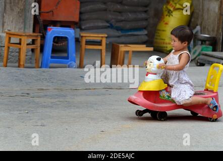 ZHAOXING DONG, Cina - 21 giugno 2012: Cinese bambino ragazza di plastica di equitazione auto in Mioa tradizionale villaggio di minoranza. Foto Stock