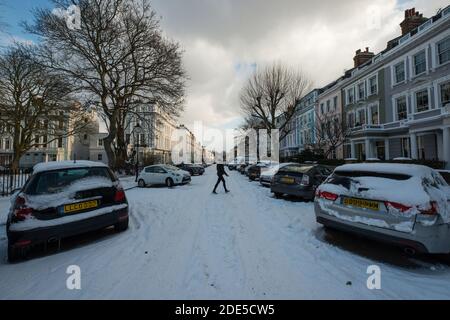 Pedone che attraversa una strada coperta di neve a Londra, Inghilterra Foto Stock