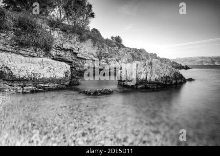 Grecia costa, acque calme, rocce, paesaggi mediterranei, Mar Ionio, vista da Kassiopi - una città greca sull'isola di Corfù. Bnw Foto Stock