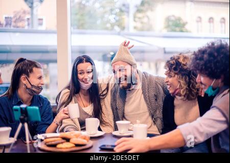 Giovani felici che condividono momenti con gli amici durante le videochiamate Indossare una maschera a faccia aperta - influencer millenari che si divertono a vlogging feed dal vivo al cof Foto Stock