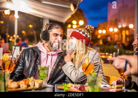 Uomo e donna sorridono in una festa al cocktail invernale Bar all'aperto con maschera a faccia aperta - nuovo stile di vita normale concetto con le persone millenarie che hanno f Foto Stock