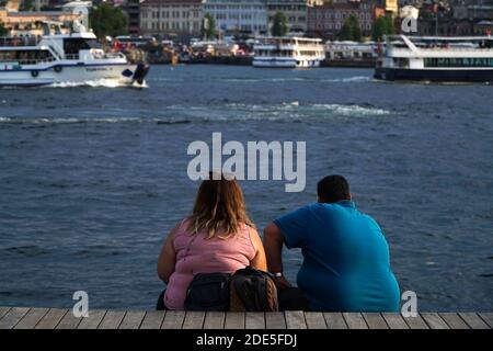 Istanbul, Turchia - 13 luglio 2019 : una giovane coppia obesa è seduta e guarda il paesaggio al Corno d'Oro, Istanbul. Ci sono anche barche da visita. Foto Stock