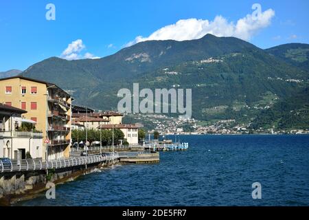 Un piccolo paese italiano con case e una strada lungo il lago. Montagne sull'altro lato del lago. Castro, Lago d'Iseo, Bergamo, Lombardia, Italia. Foto Stock