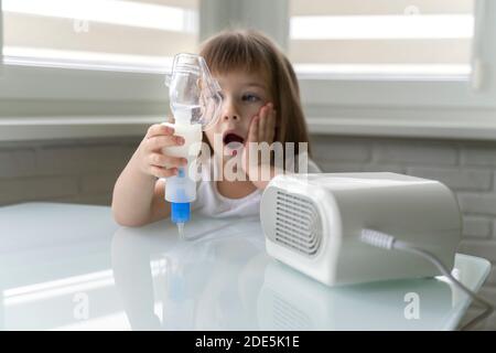 una bambina ha paura di usare un nebulizzatore. il bambino tiene una maschera in mano e non vuole inalare. fuoco su maschera, ragazza in sfocatura Foto Stock