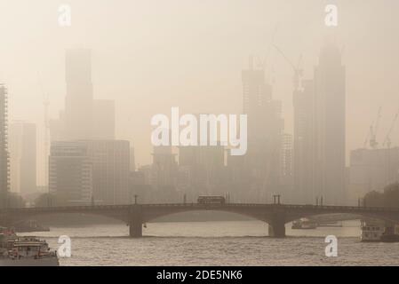 Città d'atmosfera in una nebbia arancione e un tramonto foggoso con Central London City Skyline, iconico autobus rosso di Londra che attraversa Lambeth Bridge e grattacieli e uffici, girato nel Lockdown Coronavirus Covid-19 in Inghilterra, Regno Unito Foto Stock