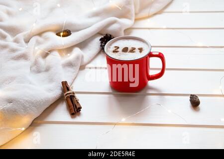 Numero 2021 su una superficie di cappuccino ghiacciato servito in una tazza rossa sull'accogliente plaid e sullo sfondo delle luci di Natale. Concetto creativo di food art per New Foto Stock