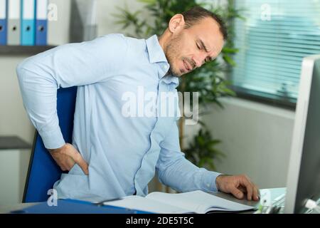 uomo con dolore alla schiena in poltrona in ufficio Foto Stock