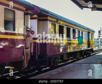 Thailandia; Febr 2020: Treno circa alla partenza da una stazione ferroviaria tailandese, ufficiale in uniforme in piedi alla porta con un cappello, uomo che mostra un fl verde Foto Stock