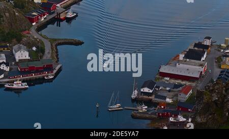 Ballstad, Vestvågøya, Lofoten, Norvegia - 08-29-2020: Veduta aerea della piccola barca con scia di onde che entrano nel porto del villaggio di pescatori Ballstad. Foto Stock