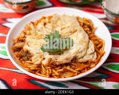 Il piatto orientale di lagman è costituito da tagliatelle fatte in casa fritte con carne, verdure ed erbe. Cucina orientale Foto Stock