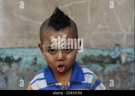 15.01.2014, Yangon, Myanmar, Asia - Ritratto di un ragazzino che stacca la lingua e che ha applicato la pasta Thanaka sul viso. Foto Stock