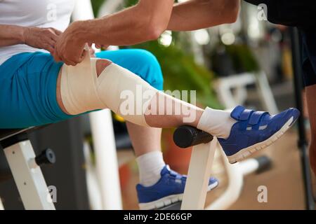 Mani maschili che avvolgono il bendaggio intorno al ginocchio. Foto Stock