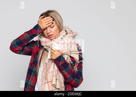 Donna in camicia controllata, sciarpa avvolta con mal di testa e vetro di tenuta con acqua, toccando la fronte e gli occhi chiusi. Stagione fredda, concetto di influenza Foto Stock