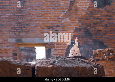 Piccola statuina bianca incontaminata di Buddha in posizione di loto che si erge tra le rovine dell'antico tempio buddista Wat Maha That, Ayutthaya storico Foto Stock