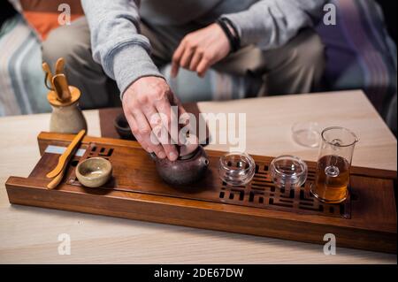 Il maestro delle cerimonie del tè versa il tè ambrato in un flusso sottile in tazze da degustazione. Primo piano con uno sfondo sfocato Foto Stock