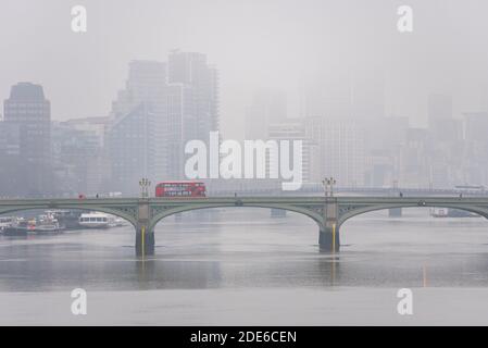 Mattina nebbia a Londra con l'autobus rosso di Londra che attraversa il ponte di Westminster. Sagome di nove blocchi di torri Elms. Skyline di Londra in nebbia. Fiume Tamigi Foto Stock