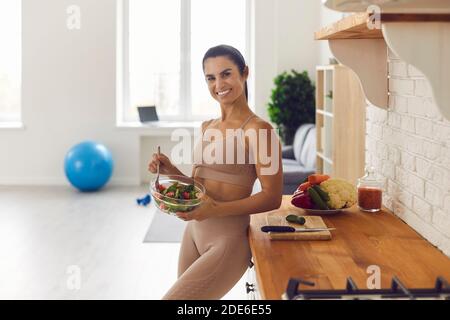 Donna atletica felice che mangia insalata vegetale sana dopo allenamento fitness a casa Foto Stock