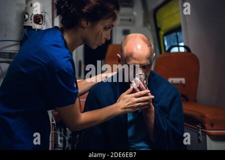 Paramedico preme una maschera di ossigeno sul viso di un uomo, che è entrato in un incidente. Foto Stock