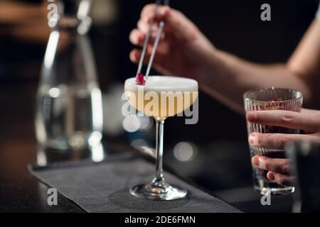 Primo piano di un bicchiere con un delizioso cocktail in piedi sul tavolo in un ristorante. Il barista crea una bevanda alcolica per le donne. Foto Stock