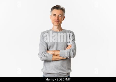 Ritratto di un uomo di mezza età sicuro che si erge su sfondo bianco, braccia incrociate sul petto e che guarda soddisfatto lo spazio sinistro della copia Foto Stock