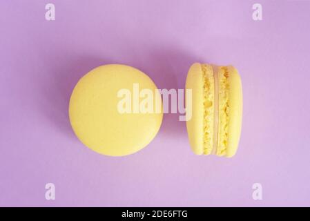 Due gustosi macaron di colore giallo francese su sfondo viola. Macaron colorati. Vista frontale. Foto Stock
