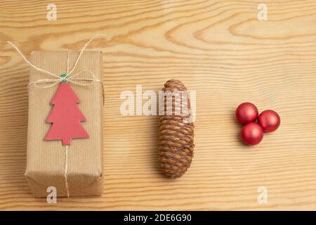 Regalo di Natale avvolto in carta riciclata adornata con l'etichetta dell'albero di natale in cartone, ananas e palline rosse. Regalo handmade.Green e sostenibile Foto Stock