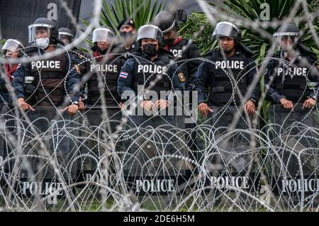 I poliziotti Riot si trovano sulla guardia dietro il recinto di filo spinato di fronte all'undicesimo cancello del Reggimento di Fanteria durante la dimostrazione. Migliaia di manifestanti pro-democrazia si sono riuniti a BTS wat phra si mahathat, dove hanno marciato verso l'undicesimo reggimento di fanteria (guardia del re) per opporsi alla legislazione di controllo su alcune unità militari da parte del re Maha Vajiralongkorn e chiedere riforme monarchiche. Foto Stock