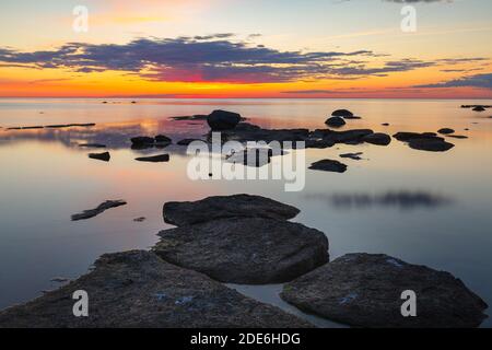 Bellissimo tramonto colorato sulla riva del mare con rocce sotto acque poco profonde Foto Stock