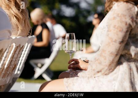 Donna Fceless seduta sulla sedia con il bicchiere di champagne in mano durante la cerimonia nuziale. Bevande alcoliche Foto Stock