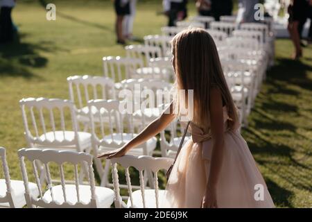 Le file di sedie bianche per gli ospiti al matrimonio e la bambina che tocca una delle sedie. Luogo per cerimonie nuziali con spazio per fotocopie. Foto Stock