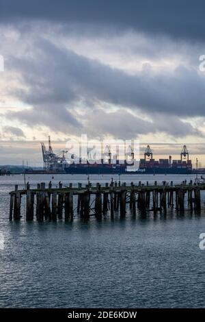 un suggestivo tramonto serale sul porto di southampton container banchine con gru e un vecchio molo in legno Foto Stock