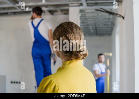 Una donna guarda il lavoro di un costruttore. Si alza con la schiena alla fotocamera Foto Stock