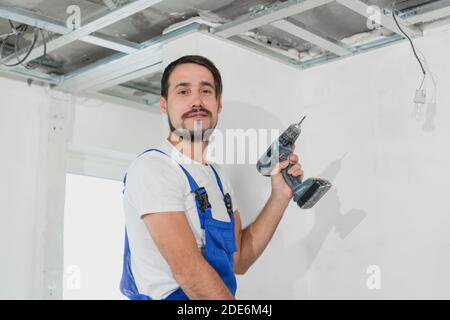 Il riparatore tiene un trapano nelle mani. Indossa tute blu Foto Stock