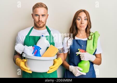 Giovane coppia di fidanzata e ragazzo che indossa grembiule tenendo prodotti e pulizia spray depresso e preoccupazione per angoscia, piangendo arrabbiato e paura. Foto Stock