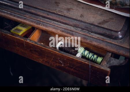 In un cassetto aperto di un vecchio tavolo di legno polveroso sono fili e aghi da cucire. Foto Stock