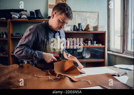 Un giovane ragazzo di talento aiuta suo padre nel commercio di famiglia, taglia fuori gli sbozzi per le scarpe dalla pelle. Foto Stock