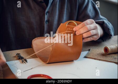 Un giovane calzolaio esperto o su misura cucina un pezzo unico di pelle in uno spazioso e luminoso studio. Foto Stock