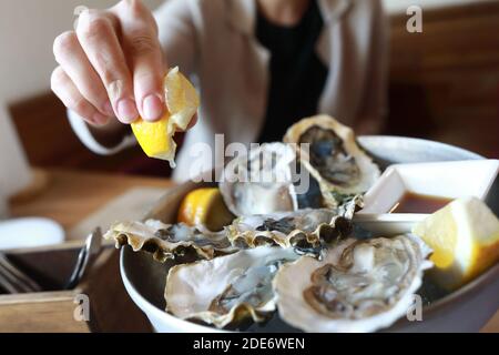 La donna spruzza le ostriche con il succo di limone nel ristorante Foto Stock
