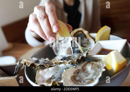 La donna spreme il succo di limone sulle ostriche del ristorante Foto Stock
