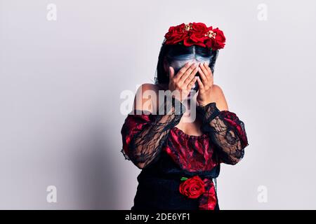 Giovane donna che indossa il giorno messicano del trucco morto con espressione triste che copre il viso con le mani mentre piange. Concetto di depressione. Foto Stock