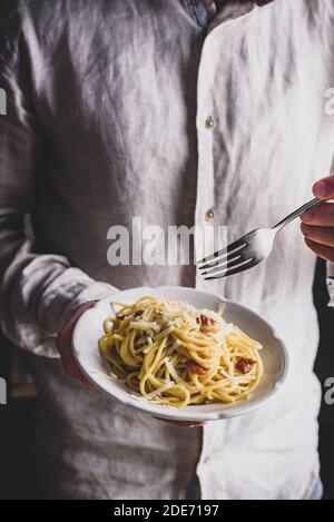 Piatto bianco con classica pasta di carbonara in mani maschili Foto Stock