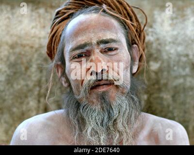 Spirituale indù indiano sadhu baba con cenere bianca sacra su tutto il viso e le spalle e con lungo dreadlock arrotolato pone per la macchina fotografica. Foto Stock