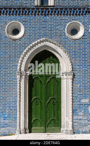 Facciata esterna di uno storico edificio gotico con un verde porta di legno e una parete di mattoni di colore blu Foto Stock