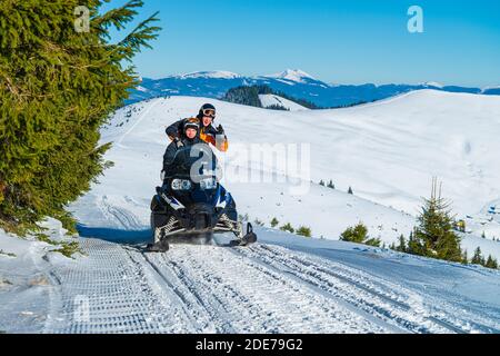 2016-12-18 Bukovel, Ucraina. Due giovani uomini in viaggio di esplorazione in motoslitta in alta montagna. Attività invernali presso la stazione sciistica Foto Stock