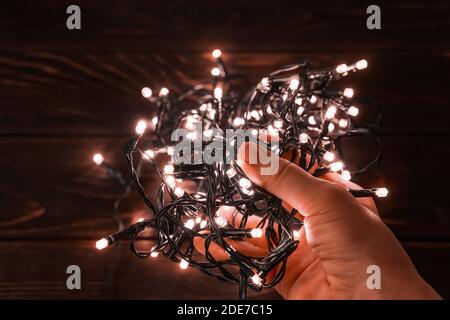 La mano della donna tiene le luci di natale scintillanti ghirlanda in un buio. Fulmine LED incandescente in un palmo. Vacanze invernali Natale e Capodanno. Foto Stock